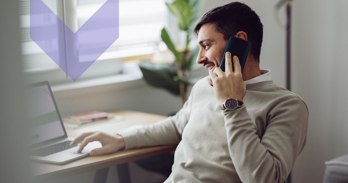 Man sitting at desk looking at screen and talking on phone. Considering IoT connectivity pricing models.
