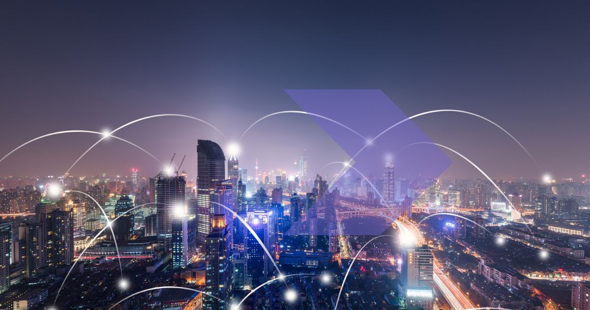 City skyline by night with purple hues. Light dots and lines emulating IoT connections in a smart city layered on the skyline. 
