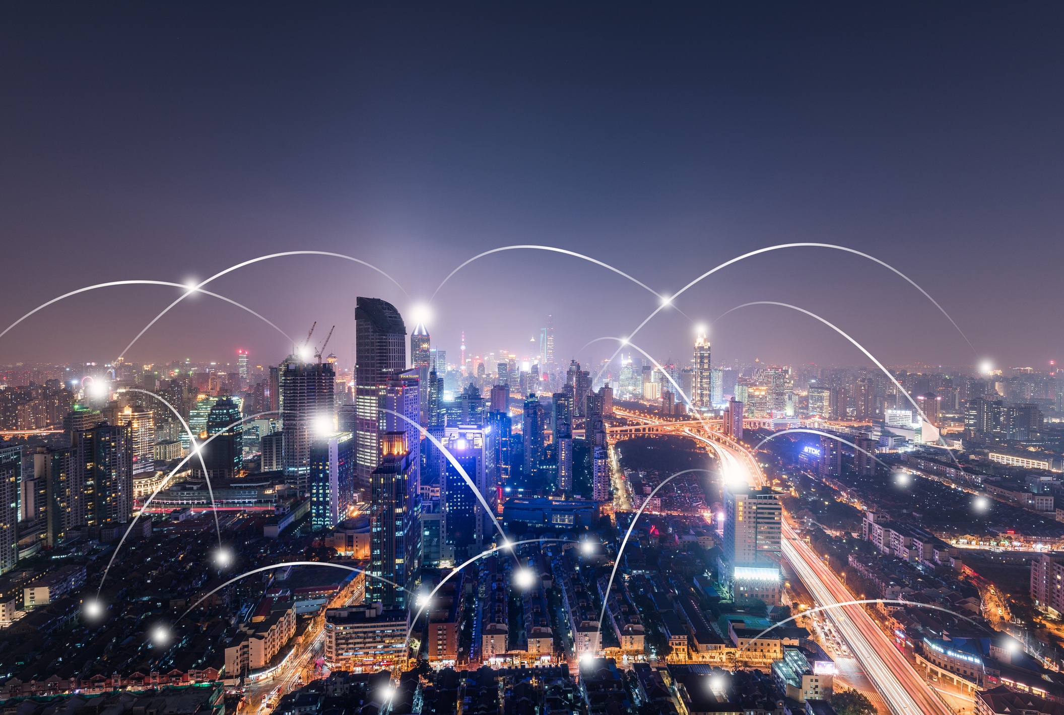 Cityscape in the dark, lit up by street lights and buildings. Shooting, bright lines from building to building illustrating connectivity between IoT devices 